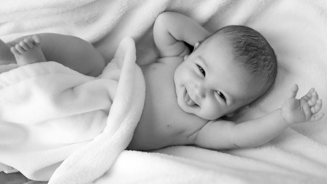 smaidošs zīdainis gultiņā, melnbalts attēls